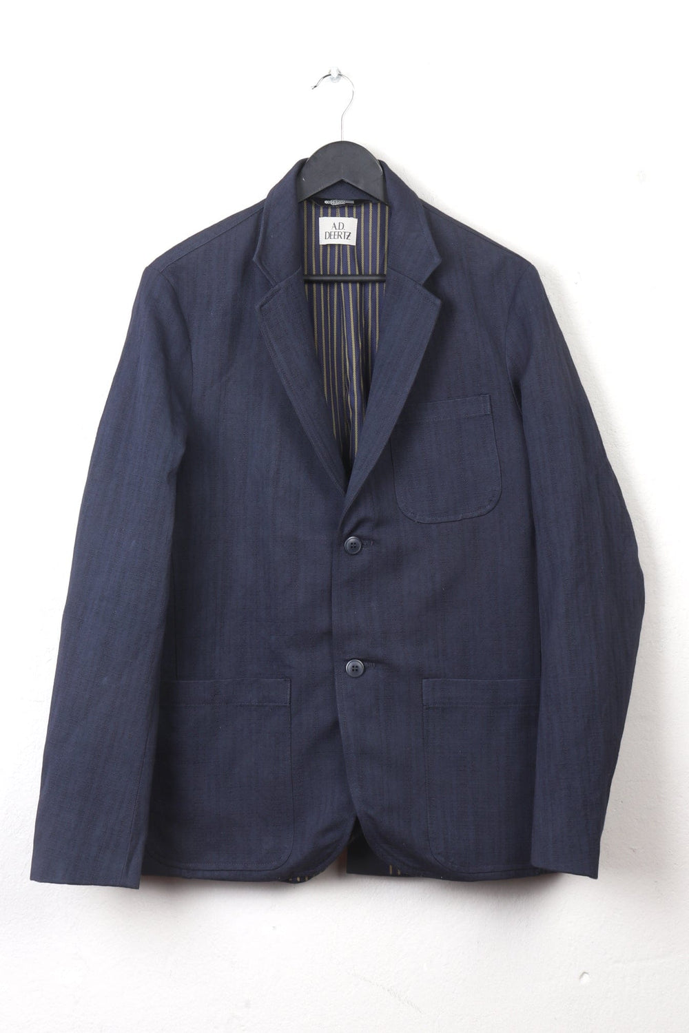 Abaca Jacket Navy hanging on a black hanger against a white background, featuring a relaxed fit with two front patch pockets and a chest pocket, made with textured navy fabric.