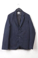 Abaca Jacket Navy hanging on a black hanger against a white background, featuring a relaxed fit with two front patch pockets and a chest pocket, made with textured navy fabric.