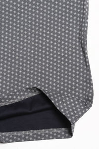 Close-up of a gray fabric with a small white geometric pattern, showing a folded hem that reveals a dark navy lining.